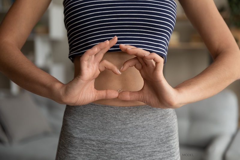 Woman framing her stomach with a heart made with her hands.