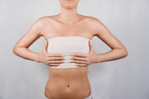 Woman with post-surgical compression bandaging around the chest area during recovery period following reduction mammaplasty procedure