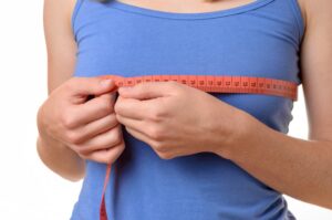 Woman measuring chest size with tape measure over blue tank top after breast reduction surgery